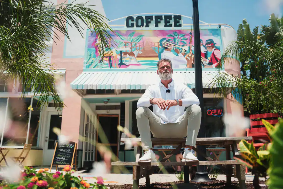 Vibrant coffee shop exterior with colorful mural, tropical plants, and welcoming open sign, showcasing a lively and inviting atmosphere for coffee lovers in a trendy neighborhood.