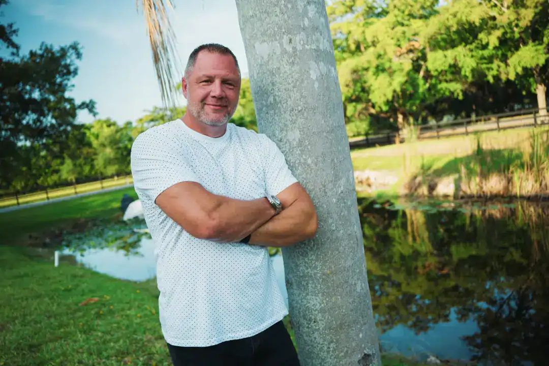 Professional man standing outdoors next to a tree in a lush park setting, representing innovation and growth for Syslo Ventures.