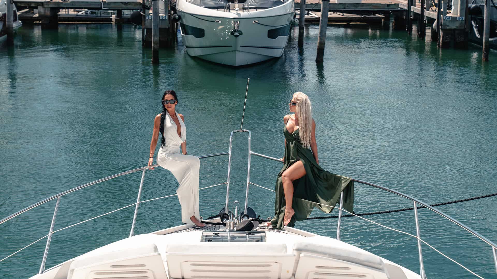 Luxurious women on yacht in marina, high-end lifestyle, fashion, leisure, nautical yacht vacation, premium boating experience, elegant summer attire, scenic harbor backdrop.