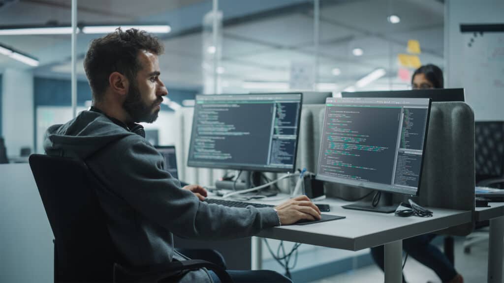 AI programmer working on code at modern office with dual monitors.