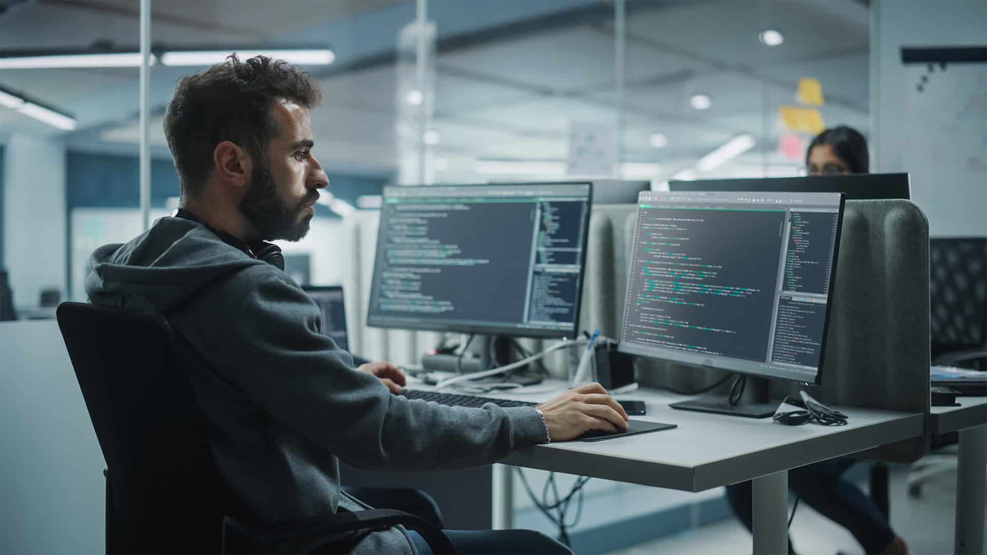 AI programmer working on code at modern office with dual monitors.