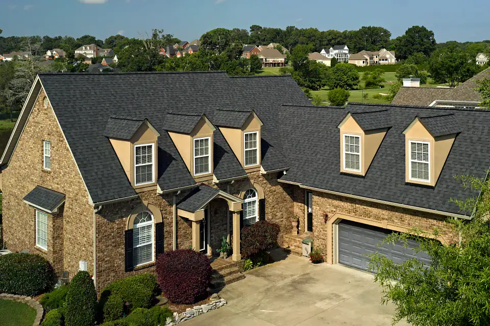 Modern brick house with black asphalt shingle roof and dormer windows in a suburban neighborhood.