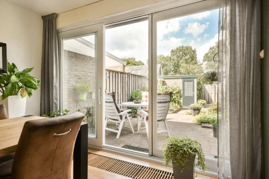 Bright indoor view of a sliding glass door leading to a backyard patio with outdoor furniture and lu.