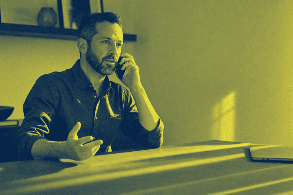 Man with beard talking on phone in modern office setting.