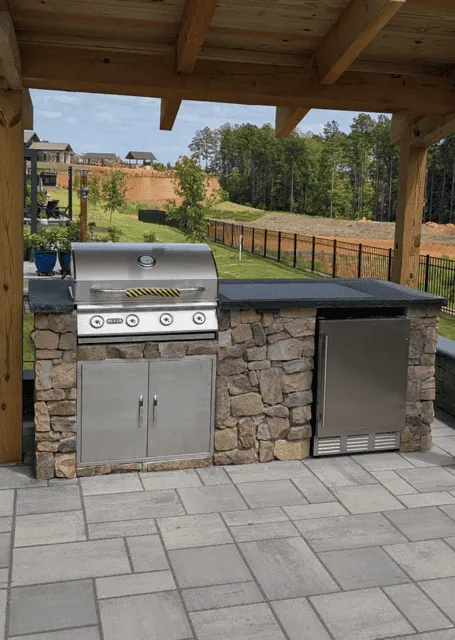 Custom outdoor kitchen in Belmont, NC featuring a 30-inch Bull Outlaw natural gas grill, Bob Timberlake Henderson thin stone veneer, natural limestone countertop, outdoor refrigerator, and paver patio.