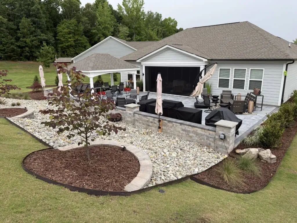 Large paver patio, seating wall, pergola, and river rock for stone drainage installation in Belmont NC by TGP Lawn and Landscape