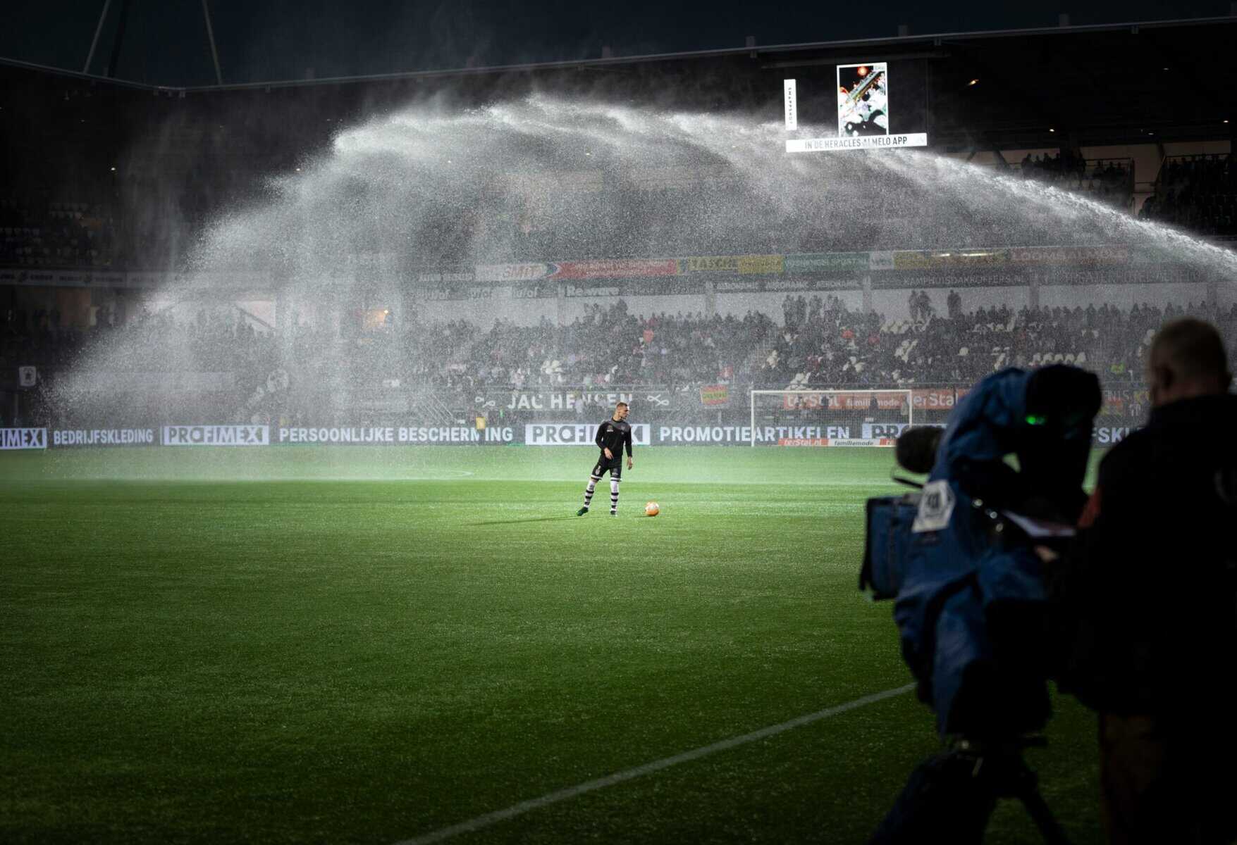Soccer player on pitch with sprinklers on