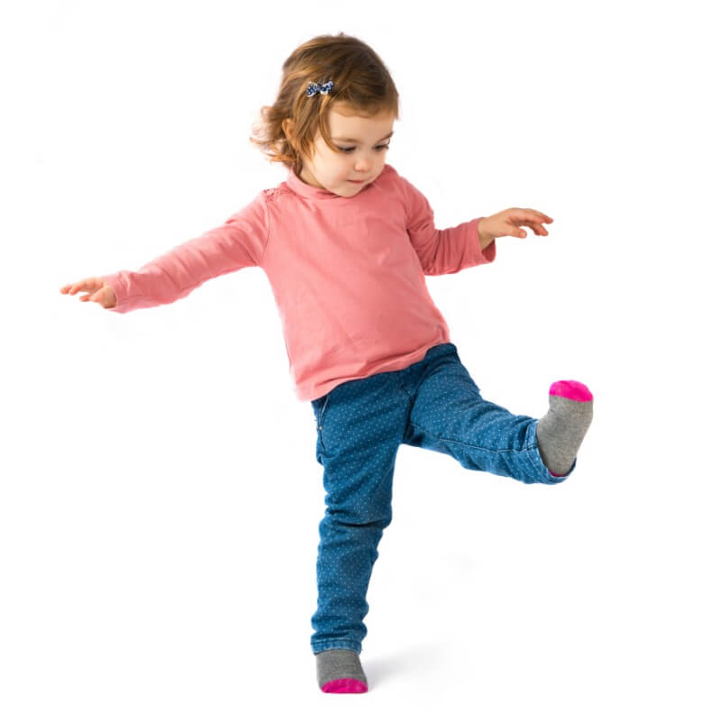 Child standing on one foot with white background. The child is performing balance activities to practice single leg stance and standing balance.