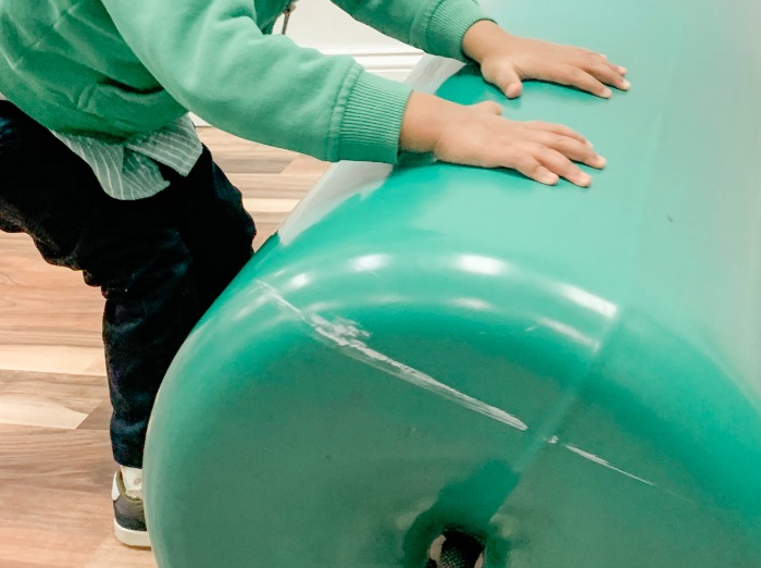 Child pushing therapy bolster with his hands.