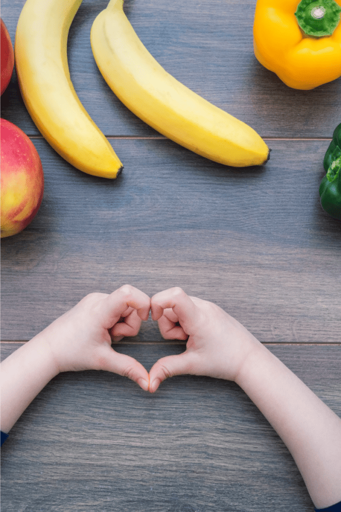 The Best Tips for Picky Eaters. Apples, bananas, peppers on a table with child's hands forming a heart.