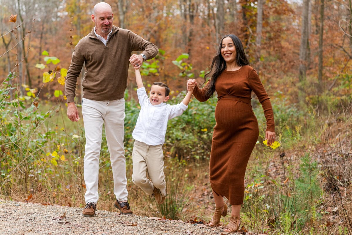 Expecting mother Sam and husband Travis swing their young son Ryan by the arms as they laugh and smile