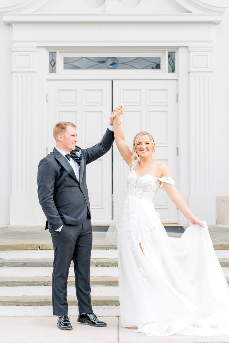 Bride and groom stand beside their wedding venue, Starmount Forest Country Club. The groom looks adoringly at his bride and spins her around for the camera.