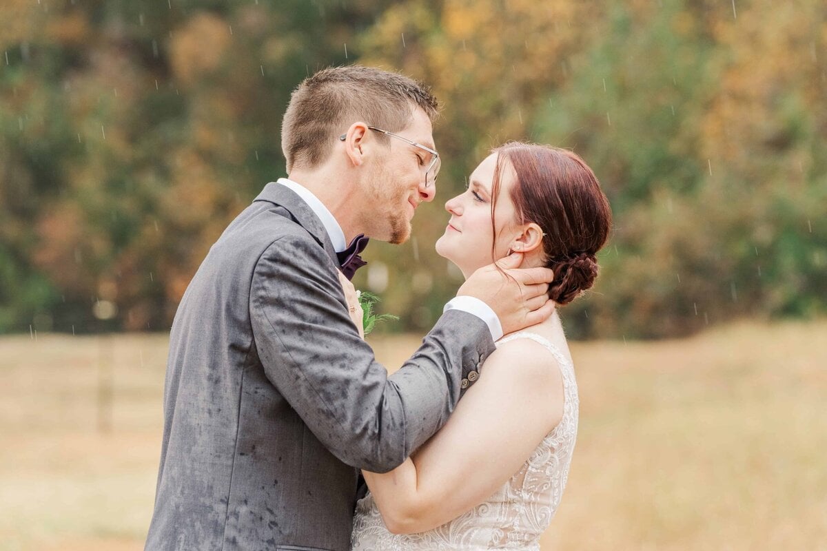 Couple sharing a kiss under clear umbrella on a rainy wedding day