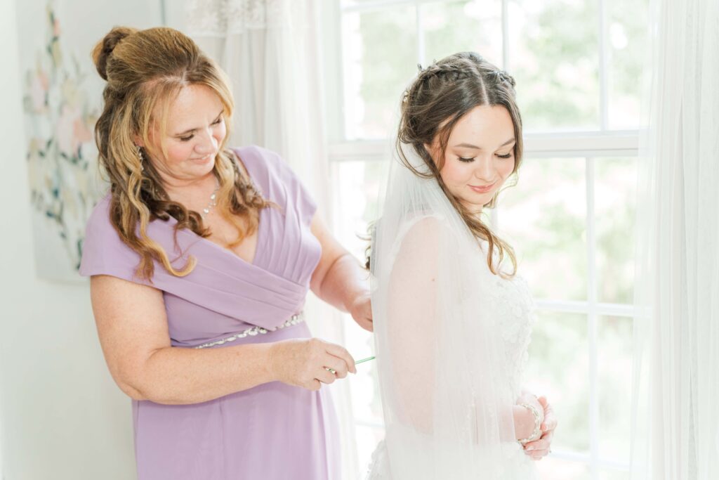 Mother of the bride buttoning up bride's dress at Heron Hill Venue