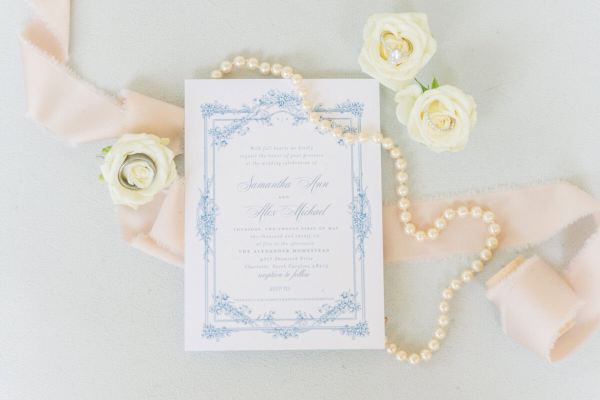 Flat lay of wedding invitations with lace bridal gown and heirloom pearl necklace, Alexander Homestead wedding details, Charlotte NC