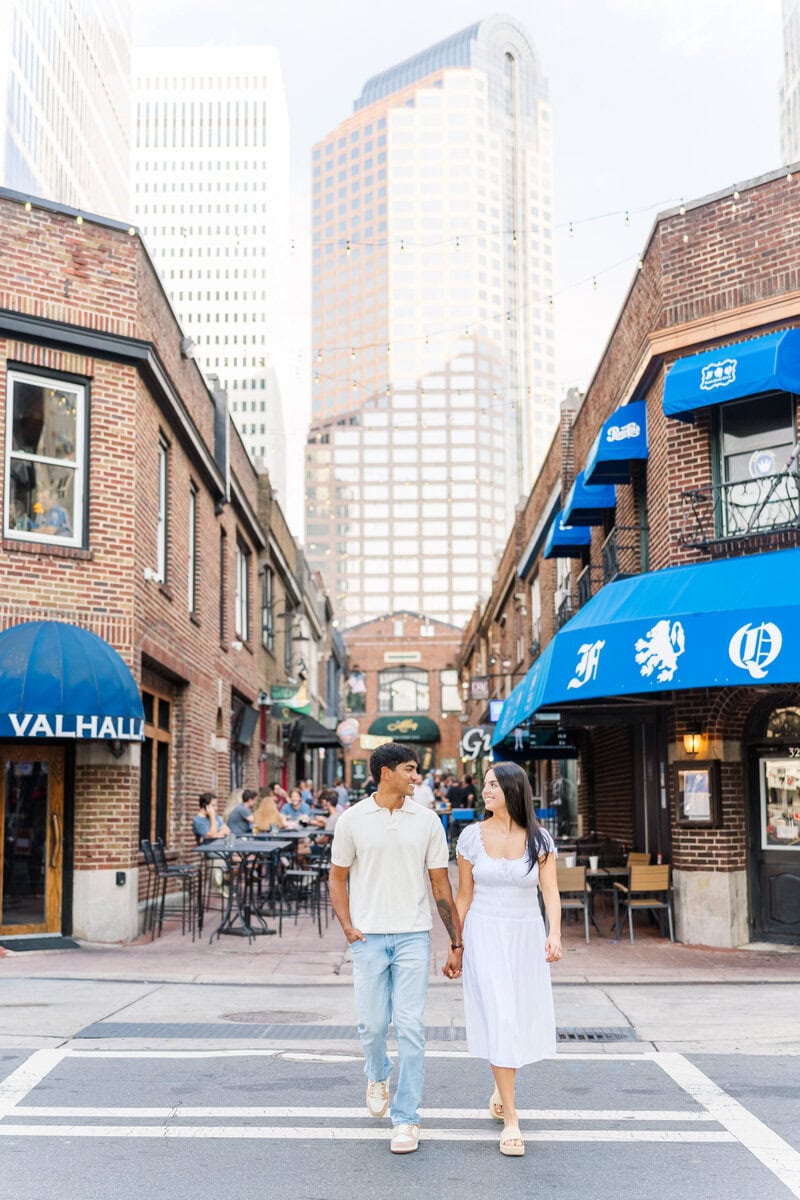 Couple walking hand in hand across brick crosswalk in Uptown Charlotte