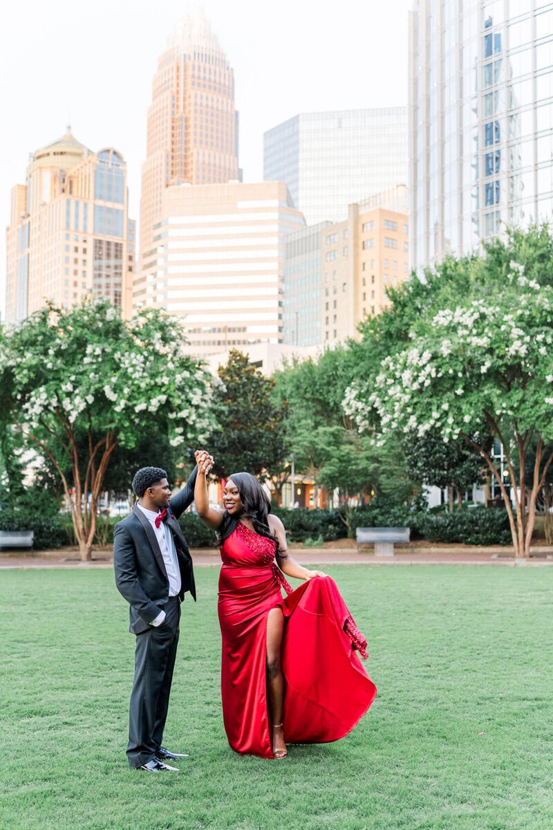 Romare Bearden Park engagement photos of couple in red dress and black suit against Charlotte skyline