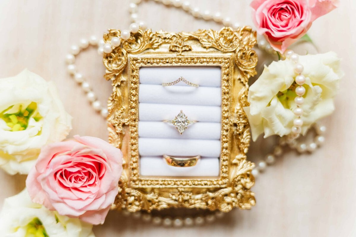 Wedding rings in a gold frame with pearls and pastel flowers at Rolling Hill Venue in Monroe NC