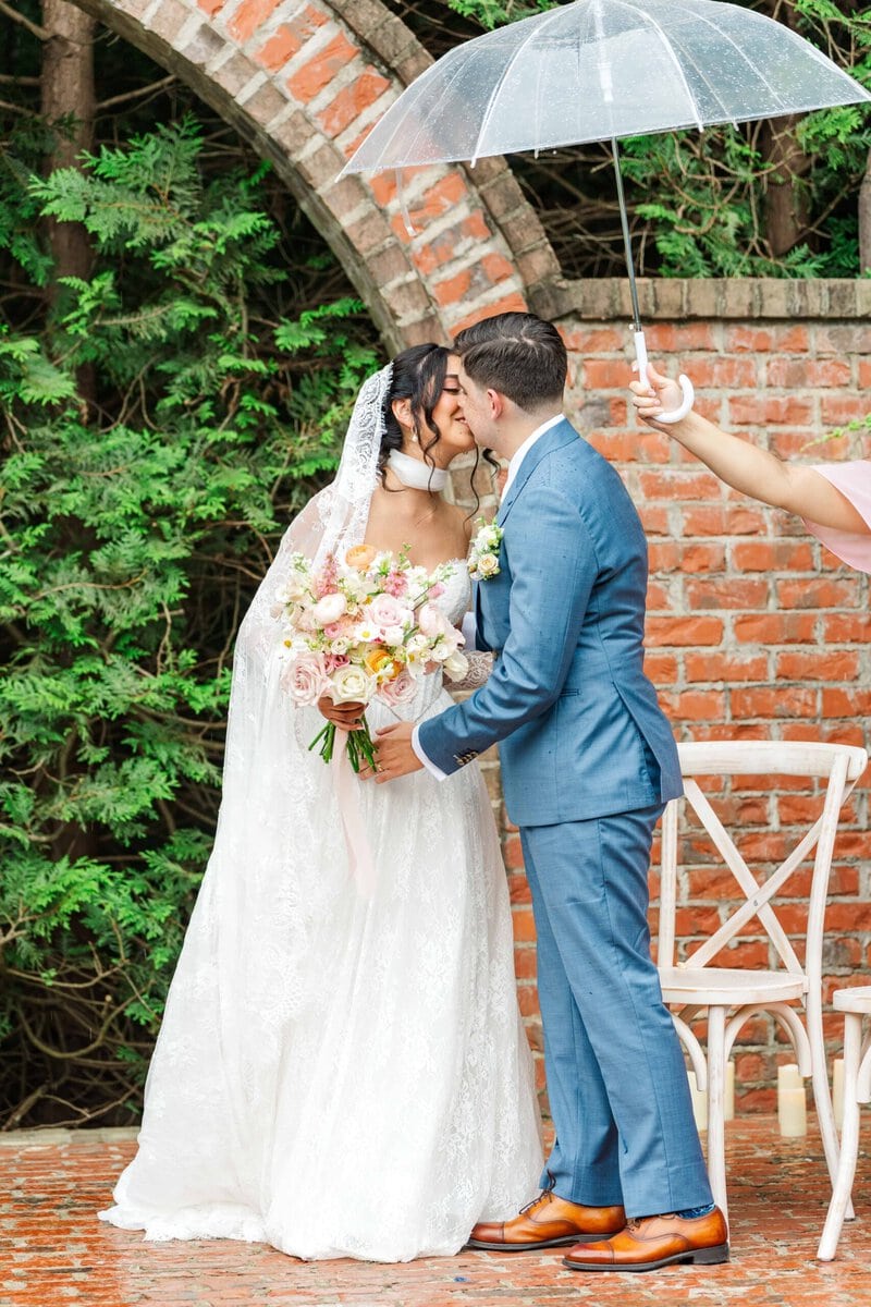 Bride and groom kissing under a clear umbrella in the rain at their Rolling Hill Venue wedding