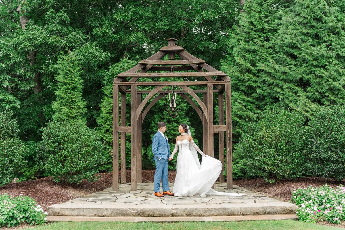 Bride and groom under the wooden pergola with a chandelier at Rolling Hill Venue