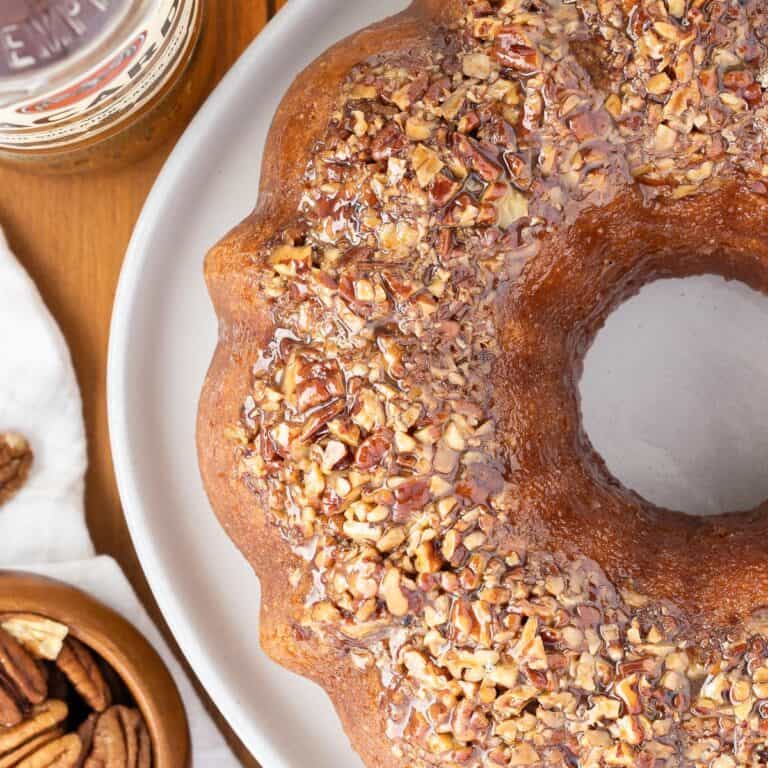 Pecan crusted Bacardi Rum Bundt Cake on a plate. A bottle of Bacardi and a bowl of pecans are off to the side.