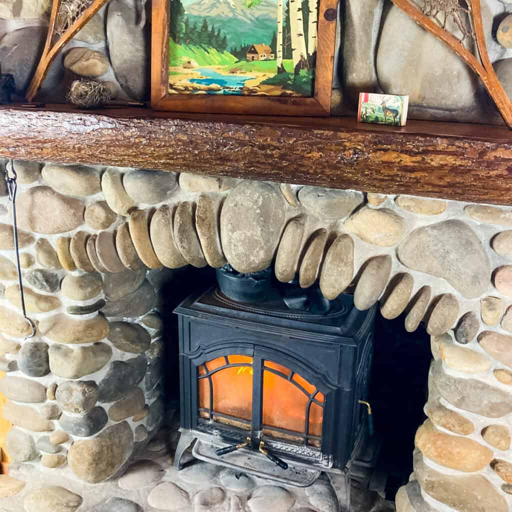 wood stove surrounded by a river rock fireplace with a cut log mantle.