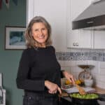 Feast Food Blog Profile Photo. Woman smiling at camera while cooking vegetables on the stove top.