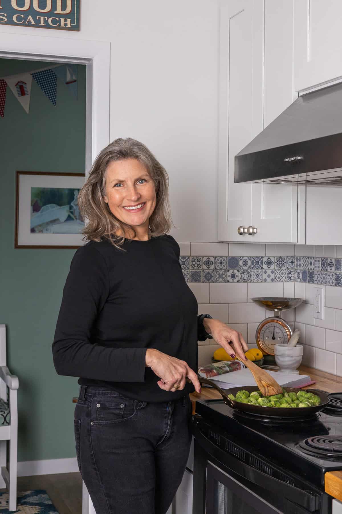 Feast Food Blog Profile Photo. Woman smiling at camera while cooking vegetables on the stove top.