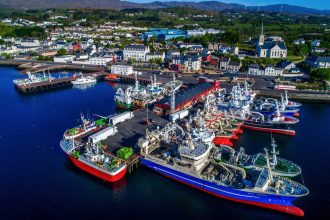 Commercial fishing vessels docked at port with industry equipment and gear visible in a coastal town.