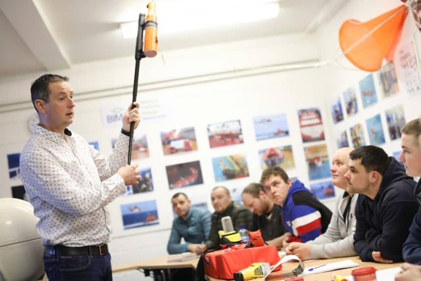 Fishermen training session in a classroom with industry equipment and vessel photos on the wall.