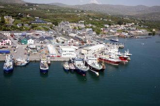 Fishing vessels docked at a busy commercial port with industry equipment and gear visible.