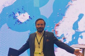 Man in suit at fishing industry conference with fishing vessel map background.