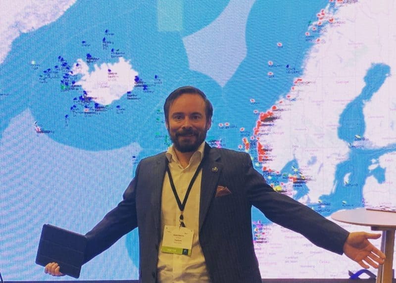 Man in suit at fishing industry conference with fishing vessel map background.