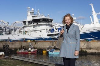 Woman standing by fishing vessels at port, commercial fishing industry publication.