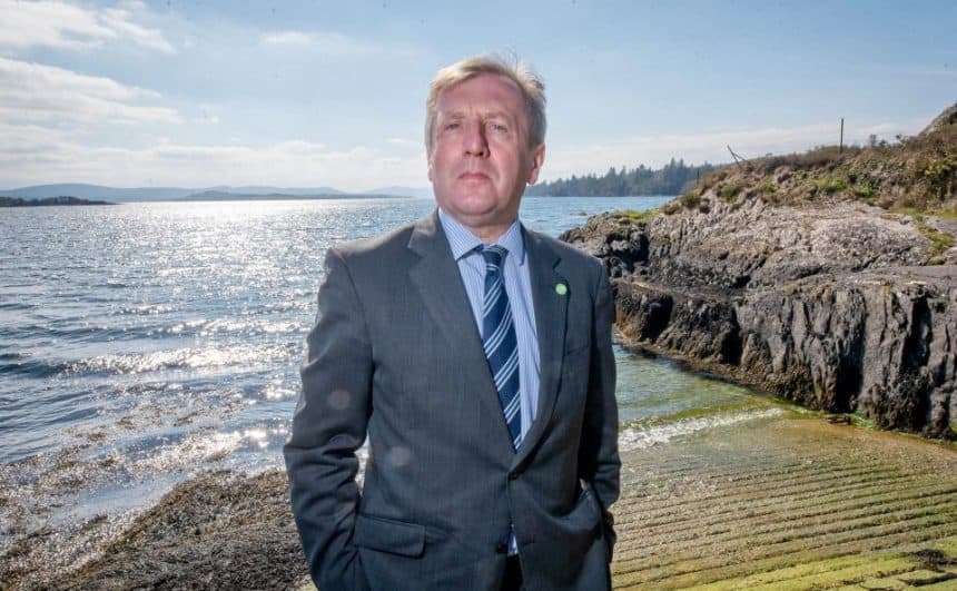 Man in suit near fishing port with fishing vessels and industry equipment in background.