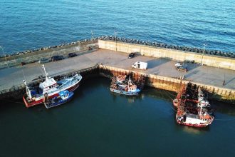 Fishing vessels docked at port in a commercial fishing industry setting, with gear and industry gear.