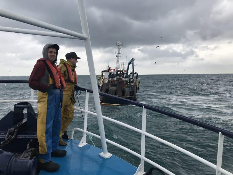 Commercial fishing vessel with fishermen on deck, industry gear, and port in background, industry-re.