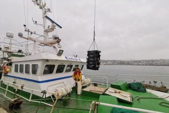 Fishing vessel with crew member and gear at port, commercial fishing industry scene.
