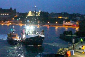 Fishing vessel being rescued at night in a commercial fishing port with industry equipment and crew.