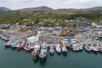 A busy fishing port with fishing vessels docked, industry equipment, and surrounding hills.