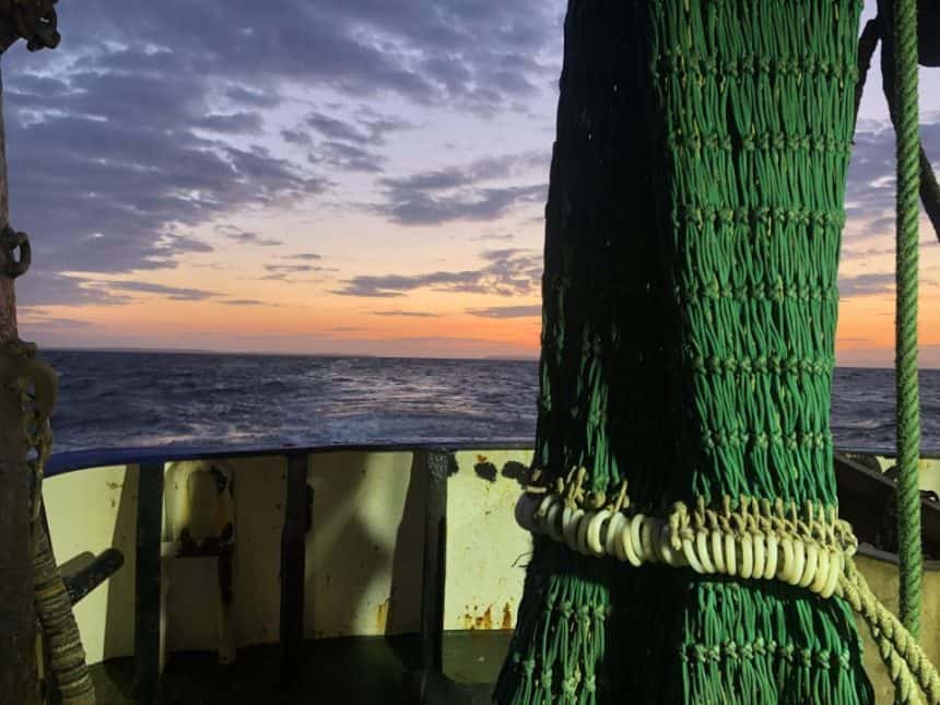 Fishing vessel at sea during sunset with gear and industry equipment visible in a commercial fishing.