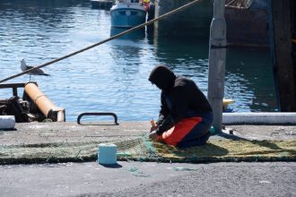Fisherman preparing fishing gear on dock at port, commercial fishing industry scene.