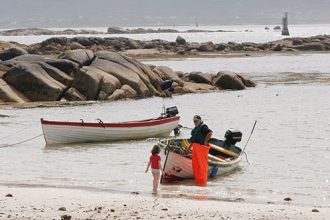 Commercial fishing vessels on the shore with crew and gear in a fishing port setting.