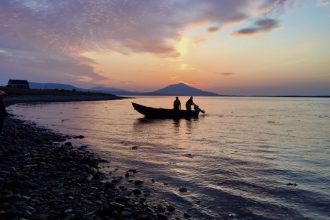 Fishing boat with fishermen at sunset in a coastal port, industry equipment visible in background.