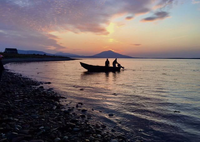 Fishing boat with fishermen at sunset in a coastal port, industry equipment visible in background.