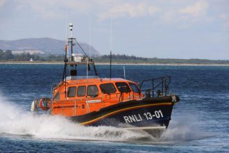 Orange RNLI rescue boat on water, commercial fishing vessel, industry equipment, safety gear, port.