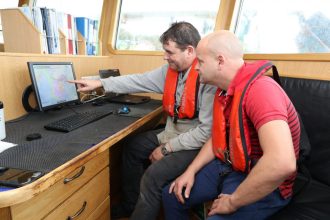 Fishermen reviewing real-time fisheries data on a vessel's navigation system in a commercial fishing.