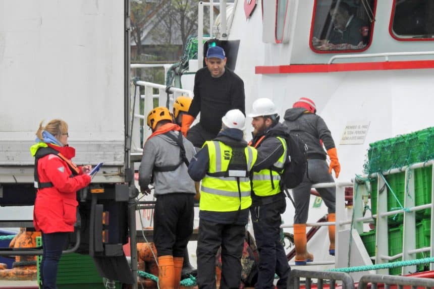 Fishermen and crew on fishing vessel deck during port operations in a commercial fishing industry.,.