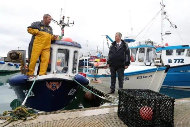 Fishing vessels docked at port with fishermen and crew members onboard, industry equipment visible.