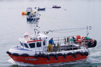 Commercial fishing vessel with crew on deck, industry gear, in port setting, October 2020.